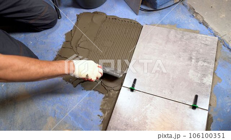 Bathroom renovation with tile adhesive. A worker lays dark gray ceramic floor tiles on an adhesive surface. Tile adhesive for bonding ceramic tiles to the floor. Applying tile adhesive to the floor 106100351