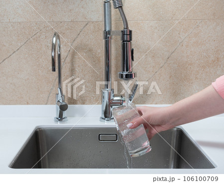 girl picking up a glass of drinking water in the kitchen girl picking up a glass of drinking water in the kitchen 106100709