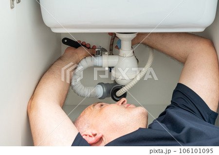 do-it-yourself plumbing repair by a man under the sink 106101095