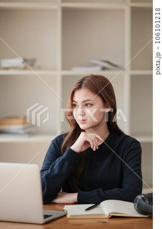 Stressed, A beautiful caucasian female student is studying remotely. She is sitting at a table at home with a laptop and a notepad and concentrated is watching a video conference lesson. 106101218