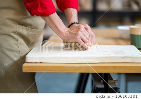 Unrecognizable woman wedging clay with hands standing behind table in studio. 106103381