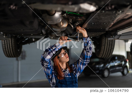 Female mechanic unscrew the nuts on the bottom of the car that is on the lift. A girl at a man's work. 106104790