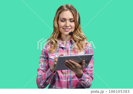 Portrait of blonde woman with headset using her tablet pc. Isolated on green background. Portrait of blonde woman with headset using her tablet pc. Isolated on green background. 106105383