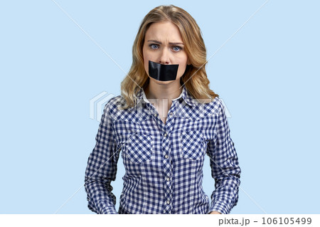 Portrait of angry stressed blond woman with mouth taped. Pastel blue background. Portrait of angry stressed blond woman with mouth taped. Pastel blue background. 106105499