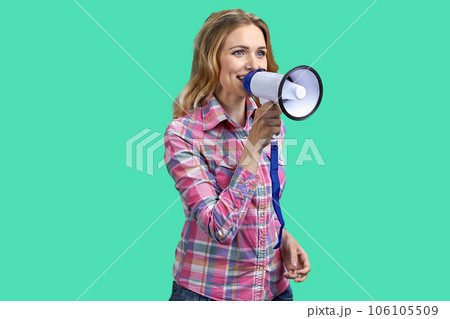 Young blonde woman holding a megaphone and speaking. Isolated on green background. 106105509