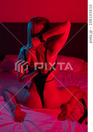 Back view of sexy blonde woman in leather bodysuit in bedroom in red blue neon light. Role-playing games. 106105610