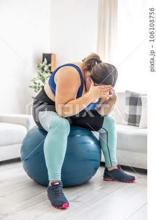 Frustrated obese woman sitting on a swiss ball and crying because of her overweight Frustrated obese woman sitting on a swiss ball and crying because of her overweight 106108756