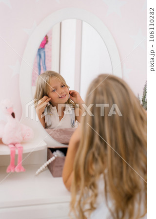 Happy child girl of seven years old puts on earrings in front of the mirror Happy child girl of seven years old puts on earrings in front of the mirror 106110282