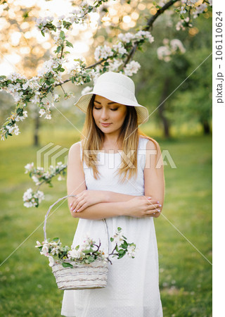 A beautiful girl in a blooming garden holds a basket with apple blossoms in her hands A beautiful girl in a blooming garden holds a basket with apple blossoms in her hands 106110624