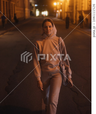 Caucasian woman walks along road through city in evening in light of lanterns Caucasian woman walks along road through city in evening in light of lanterns 106111526