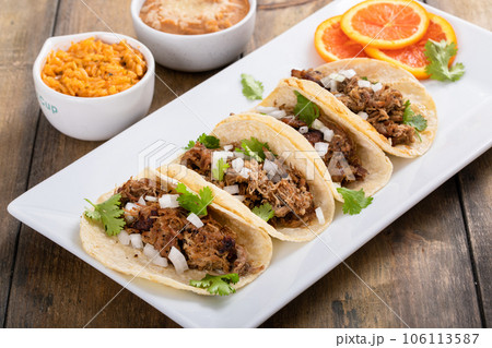 Pork carnitas tacos with onion and cilantro served with rice and refried beans 106113587