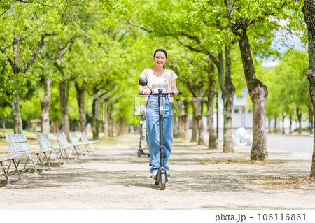 緑が美しい並木道を電動キックボードで爽快に走る若くてかわいい女性|電動キックボードイメージ 緑が美しい並木道を電動キックボードで爽快に走る若くてかわいい女性|電動キックボードイメージ 106116861