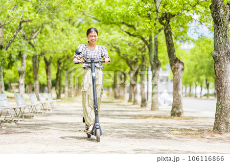 緑が美しい並木道を電動キックボードで爽快に走る若くてかわいい女性|電動キックボードイメージ 緑が美しい並木道を電動キックボードで爽快に走る若くてかわいい女性|電動キックボードイメージ 106116866