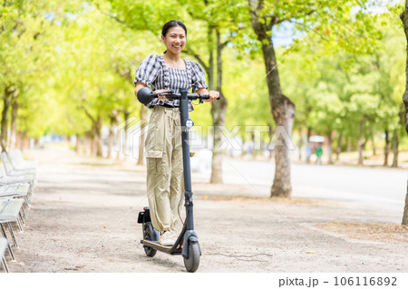 緑が美しい並木道を電動キックボードで爽快に走る若くてかわいい女性|電動キックボードイメージ 緑が美しい並木道を電動キックボードで爽快に走る若くてかわいい女性|電動キックボードイメージ 106116892