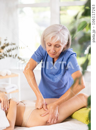 Mature masseur performs stroking and patting during spa procedure of thigh area for female Mature masseur performs stroking and patting during spa procedure of thigh area for female 106117263