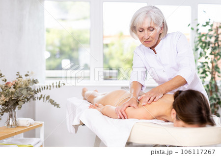 Elderly woman doing back massage to young woman Elderly woman doing back massage to young woman 106117267