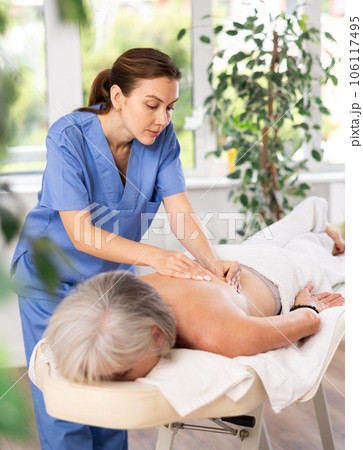 Unrecognizable elderly woman lies face down on couch and enjoy spa treatments, shoulder massage Unrecognizable elderly woman lies face down on couch and enjoy spa treatments, shoulder massage 106117495