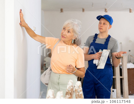 Mature woman checks the quality of plastered wall in room being renovated Mature woman checks the quality of plastered wall in room being renovated 106117548