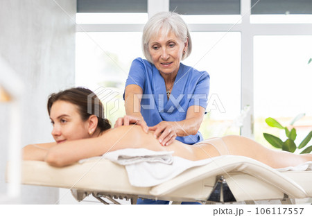 Experienced older professional masseuse doing back massage to young woman 106117557