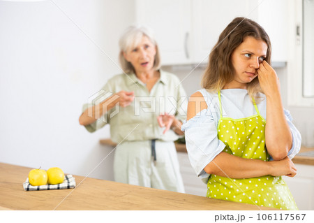 Upset girl at home kitchen while worried elderly mother reprimanding her. Family conflicts concept Upset girl at home kitchen while worried elderly mother reprimanding her. Family conflicts concept 106117567