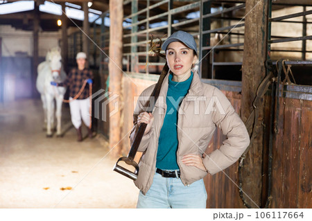 Woman with pitchfork standing in horse barn 106117664