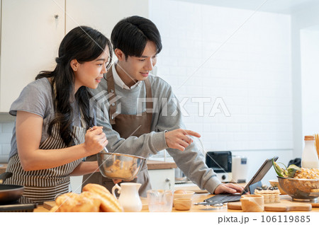 A lovely Asian couple is reading a pastry recipe on a tablet, enjoying cooking dates at home 106119885