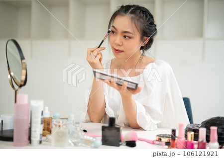 A beautiful Asian woman applies eye shadow to her eyelids, getting ready 106121921