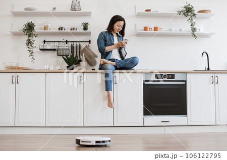 Lady scrolling on mobile while robot dust collector cleaning 106122795