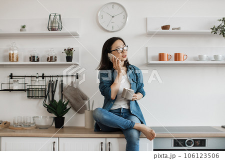 Female resting on kitchen set while talking on smartphone 106123506