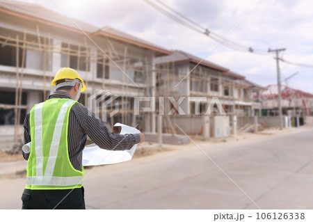 young professional engineer in protective helmet and blueprints paper at the house building construction site 106126338