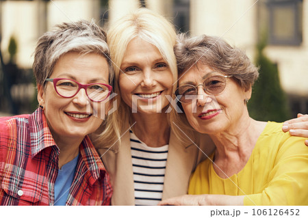 Smiling middle age women hug and look at camera on city street. Female friendship 106126452
