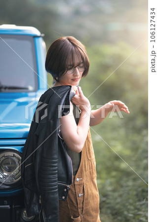 青い車にもたれて足元を見てる女性 106127434
