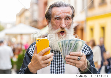 Happy elderly man counting money dollar cash, use smartphone calculator app in urban city street 106131064