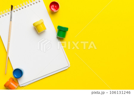Album pages and paints, pencils, brush on a colored background. Top view with empty space. workplace for creativity. home teaching concept drawing 106131246