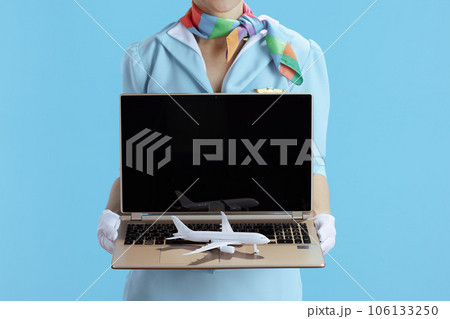 Stylish female stewardess on blue showing laptop blank screen Stylish female stewardess on blue showing laptop blank screen 106133250