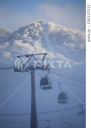 靄の切れ目から見えるゴンドラと山の斜面のゲレンデ 106133511