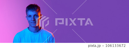 Handsome young guy with cute smile looking at camera against gradient pink purple background in neon light Handsome young guy with cute smile looking at camera against gradient pink purple background in neon light 106133672