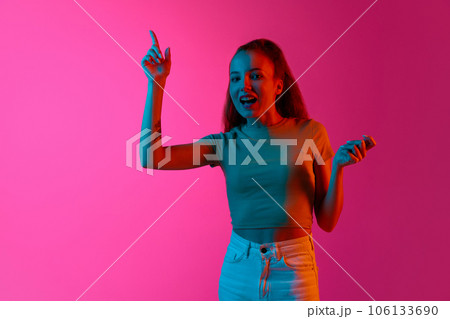 Emotional and excited girl raisin ginger up against pink studio background in neon light. Creative ideas 106133690
