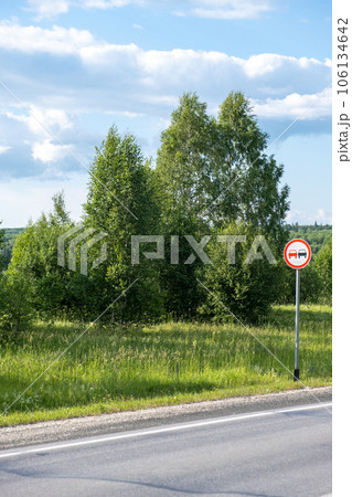 A road sign Overtaking is prohibited on a suburban highway through the forest on a sunny summer day. Beautiful landscape of nature and road. 106134642