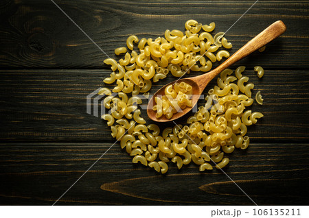 Scattered raw pasta on a vintage table and in a wooden spoon. The concept of cooking pasta on the kitchen table. Black space for menu or recipe Scattered raw pasta on a vintage table and in a wooden spoon. The concept of cooking pasta on the kitchen table. Black space for menu or recipe 106135211