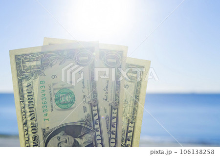 Three denominations of US dollars banknotes with face value of one dollar on background of sea waves on sandy beach of the seashore on a sunny summer day. Concept money finance 106138258