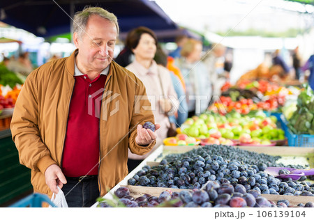 Elderly man buys plums at an open-air market Elderly man buys plums at an open-air market 106139104