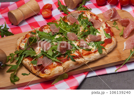 roman pizza with jamon and arugula on a wooden board roman pizza with jamon and arugula on a wooden board 106139240