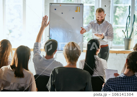 Male speaker giving talk at business meeting. Audience in conference hall. Rear view of businessman raising hand for speaker's question. 106141304