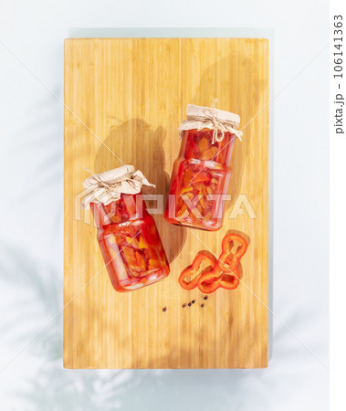 Probiotic food. Pickled or fermented vegetables. Lecho, sweet peppers in glass jars on a wooden board with shadows and copy space. Mockup of food preserving or canning. Close up, flat lay 106141363