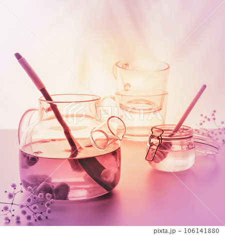 Blurred summer relax tea composition with glass teapot, jar with honey and two glass cups on light sunset background with palm shadows. Healthy no alcohol natural calm drink. Very Peri coloristic 106141880