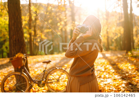 Beautiful young woman takes photos with a retro camera in autumn forest. Enjoying autumn weather. Beautiful young woman takes photos with a retro camera in autumn forest. Enjoying autumn weather. 106142465