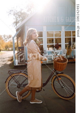 Beautiful woman with a bike on the background of a blue house in the fall. Beautiful woman with a bike on the background of a blue house in the fall. 106142491