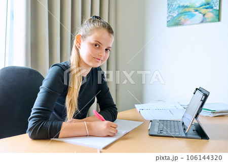 Portrait of smiling child girl sitting at desk at home with digital tablet textbooks 106144320