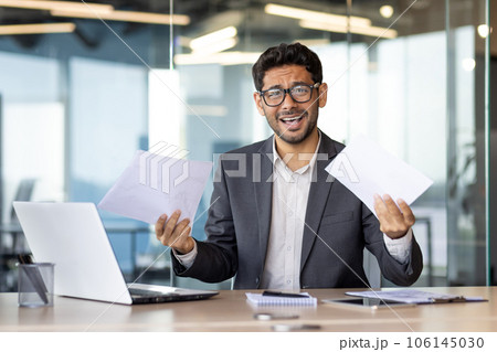 Upset and disappointed businessman financier investor looking at camera, man holding papers reports and contracts, unhappy with bank achievement results inside office with laptop. Upset and disappointed businessman financier investor looking at camera, man holding papers reports and contracts, unhappy with bank achievement results inside office with laptop. 106145030